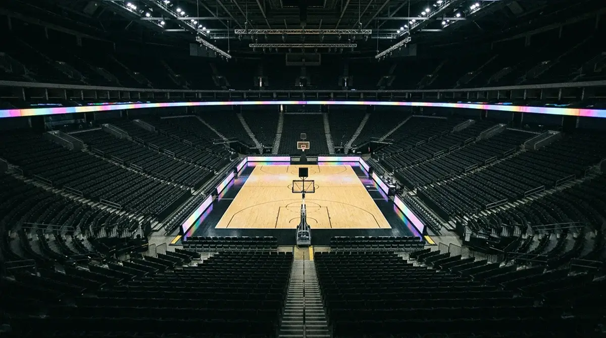 Professional basketball arena with hardwood court under bright lights before a game with empty stands and scoreboards visible